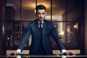 Confident young man standing with hands on the table to suggest the psychology of fashion.