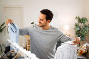 Man looking at last year's summer clothes on hangers at home.