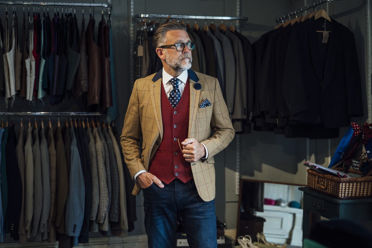 Man dressed formally in a waistcoat and suit jacket standing in front of a timeless wardrobe.