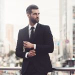 Confident young man in a suit adjusting his sleeve and looking away while standing outdoors, making the best first impression.