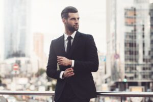 Confident young man in a suit adjusting his sleeve and looking away while standing outdoors, making the best first impression.