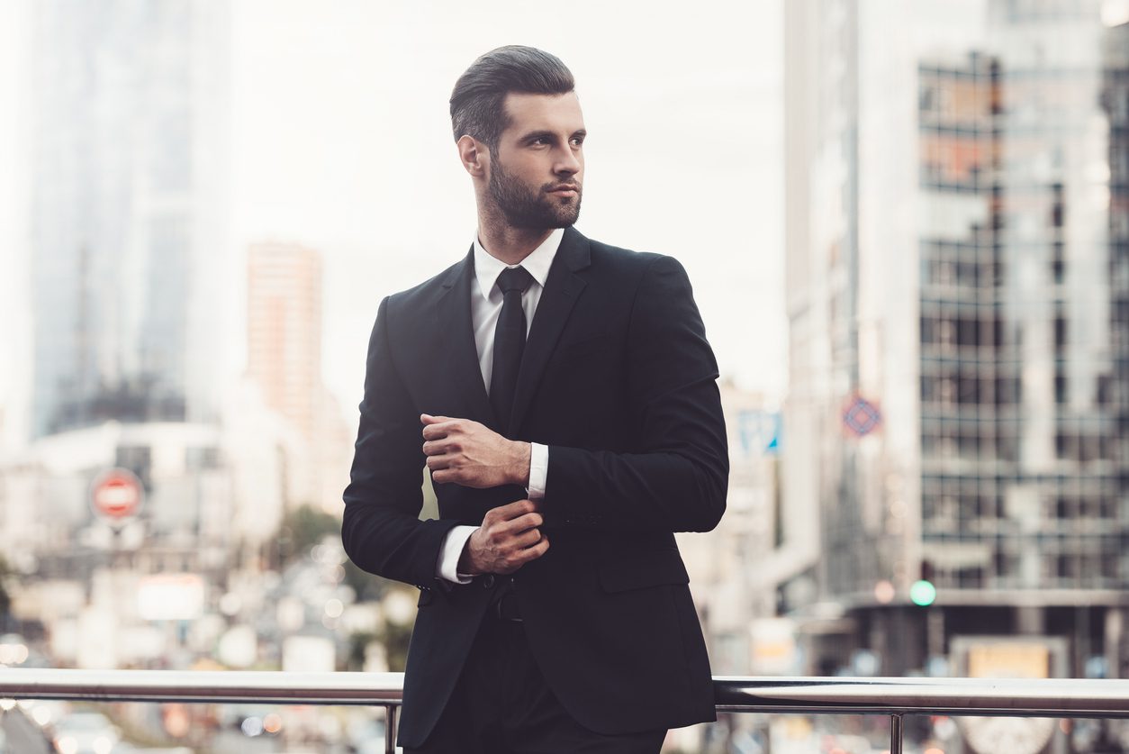 Confident young man in a suit adjusting his sleeve and looking away while standing outdoors, making the best first impression.