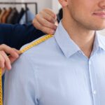 Tailor measuring man's shoulder, making tailored clothing in a shop.